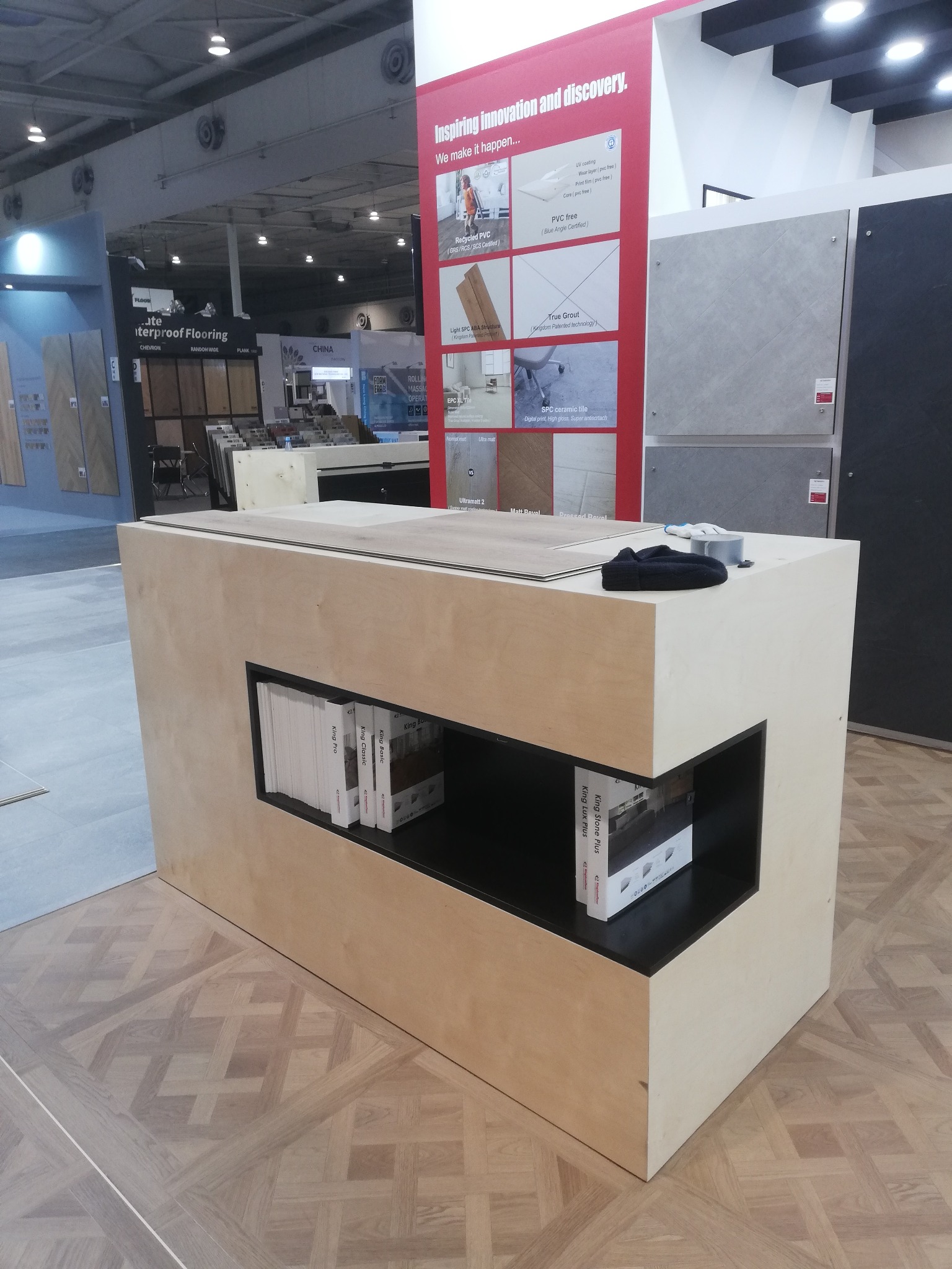 Ekspozycja paneli podłogowych na stoisku targowym z próbkami i materiałami informacyjnymi. Widoczny wzór parkietu na podłodze i elementy stoiska.