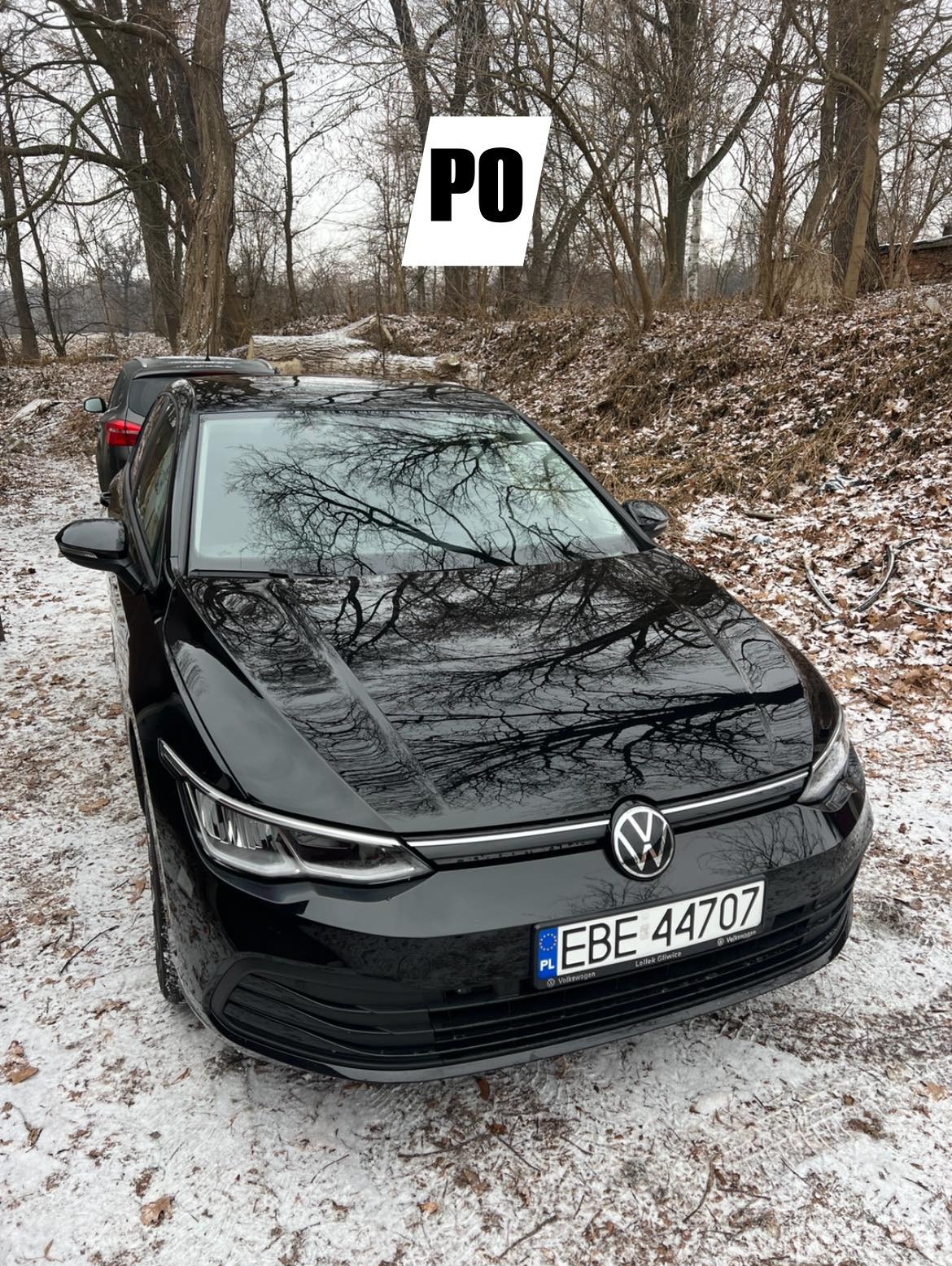 Błyszczący, czarny Volkswagen Golf po detailingu, zaparkowany na śniegu. Na masce odbijają się gałęzie drzew. Tablica rejestracyjna EBE 44707.