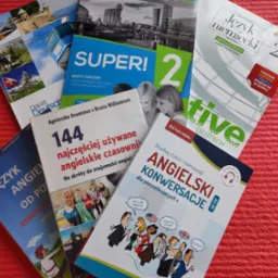 Kolorowe podręczniki do nauki języków: angielskiego, niemieckiego, ułożone na czerwonym tle. Widoczne tytuły i okładki książek.