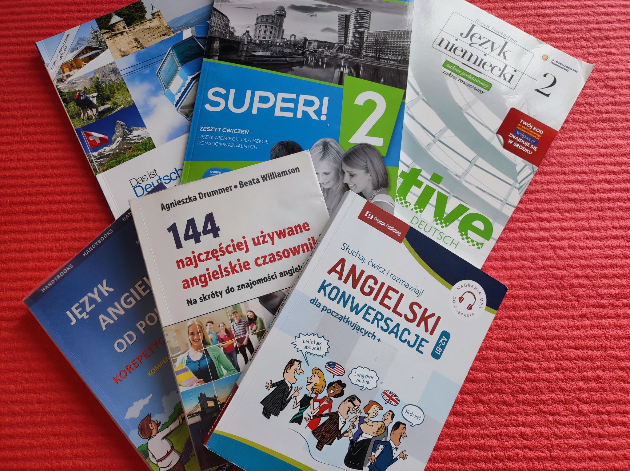 Kolorowe podręczniki do nauki języków: angielskiego, niemieckiego, ułożone na czerwonym tle. Widoczne tytuły i okładki książek.