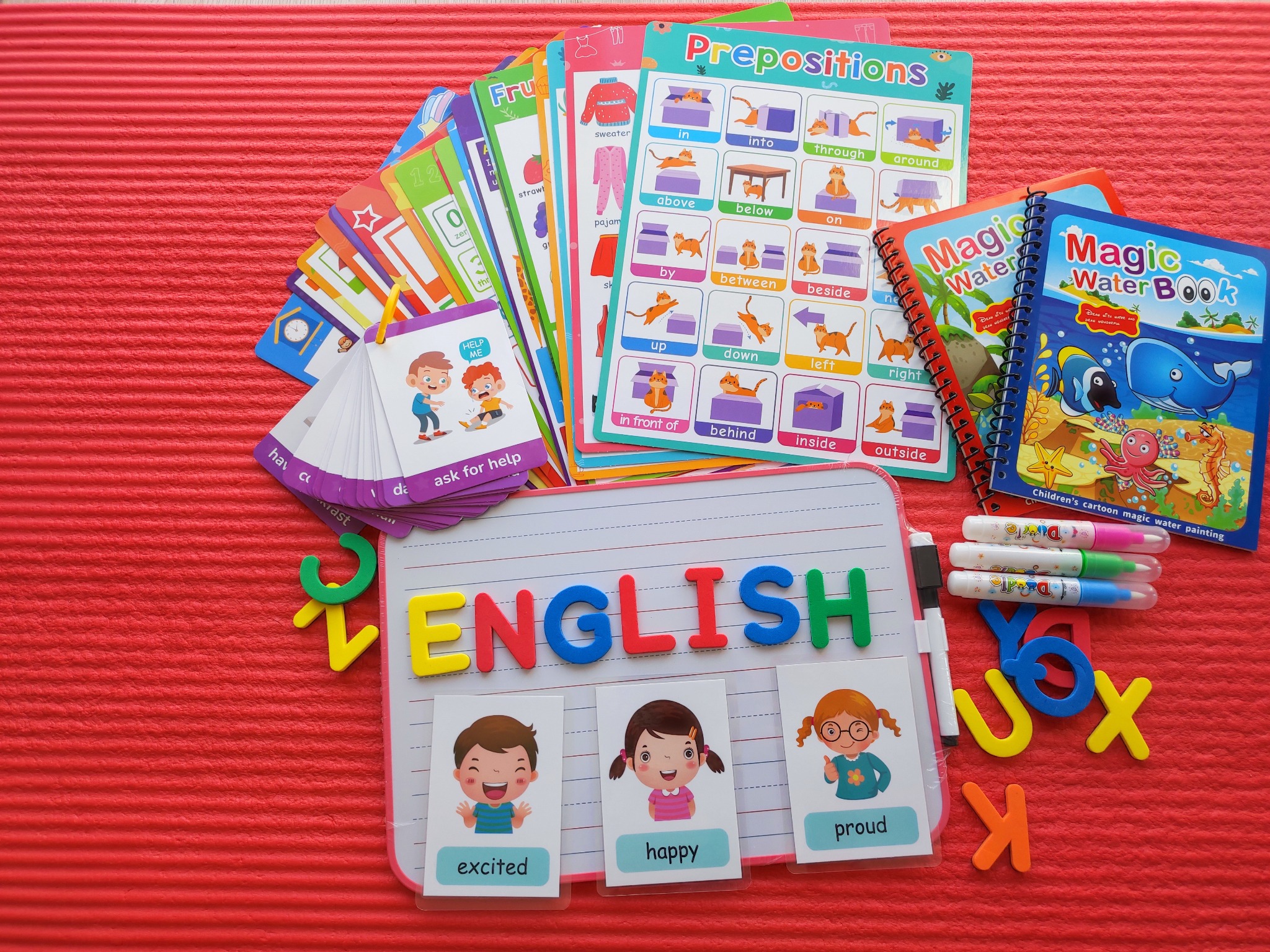 Materiały edukacyjne do nauki angielskiego: tablica z napisem 'English', karty obrazkowe z emocjami, książki do malowania wodą i karty z gramatyką.
