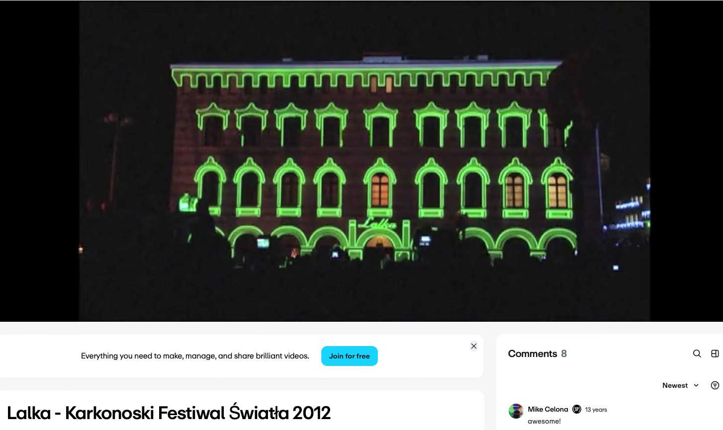 Fasada budynku oświetlona zielonymi neonami podczas festiwalu światła. W tle ciemne niebo i sylwetki obserwujących. Nocne ujęcie.