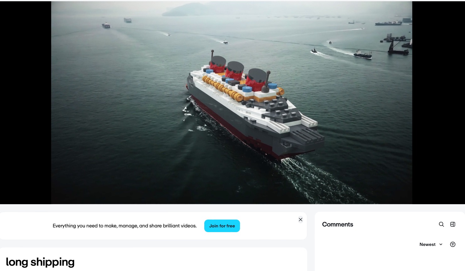 Filmowy kadr z drona: model statku pasażerskiego z klocków LEGO płynie po spokojnym morzu. W tle inne statki i zarys lądu we mgle.