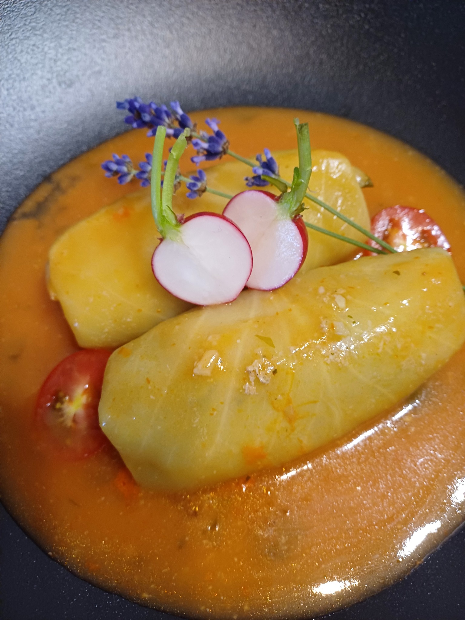 Elegancko podane gołąbki w sosie pomidorowym, udekorowane rzodkiewką, pomidorem i gałązką lawendy na czarnym talerzu. Danie cateringowe.