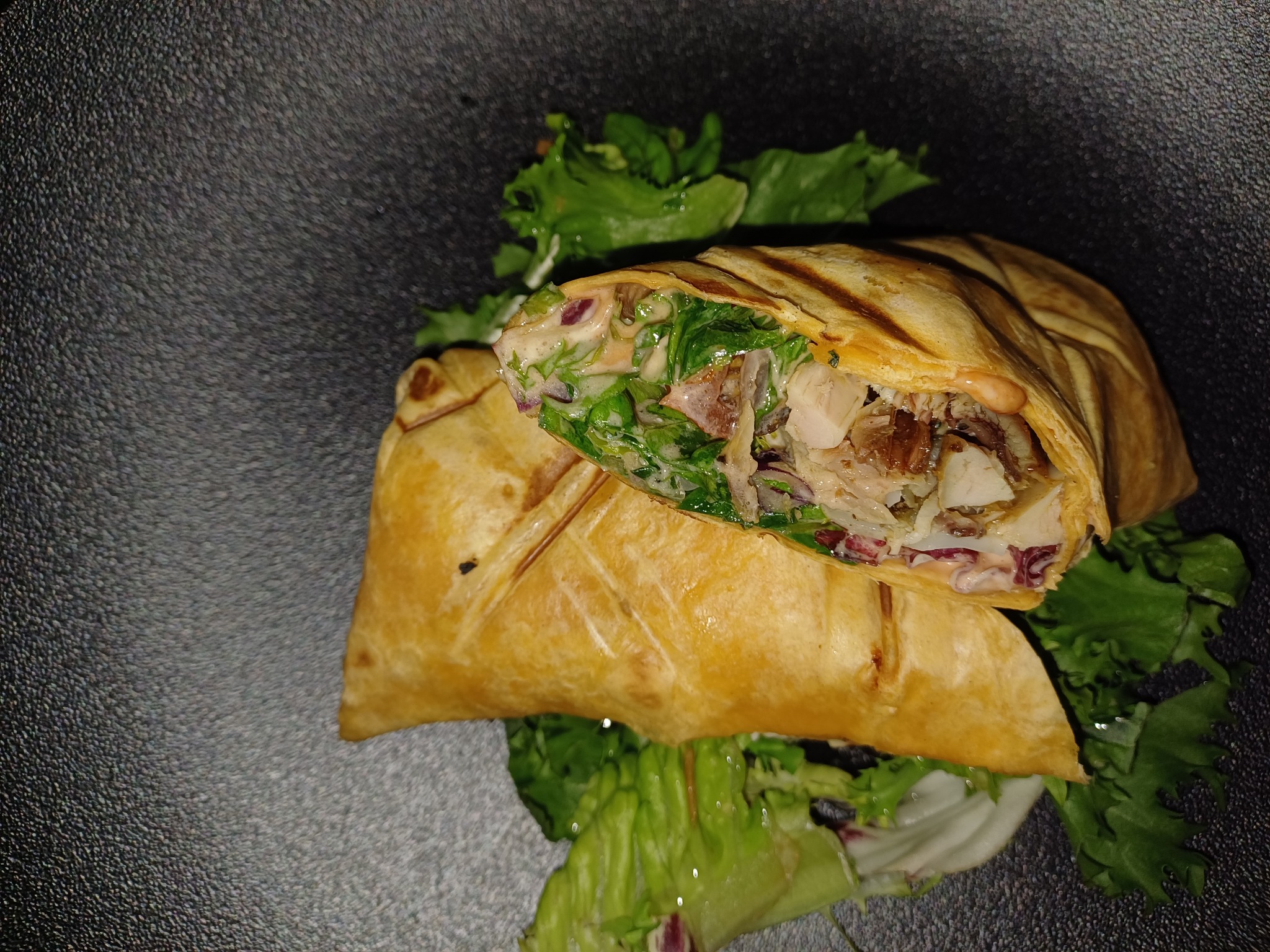 Dwa przekrojone wrapy z grillowaną tortillą, kurczakiem, warzywami i sosem, ułożone na świeżej sałacie na ciemnym tle, prezentacja cateringu.