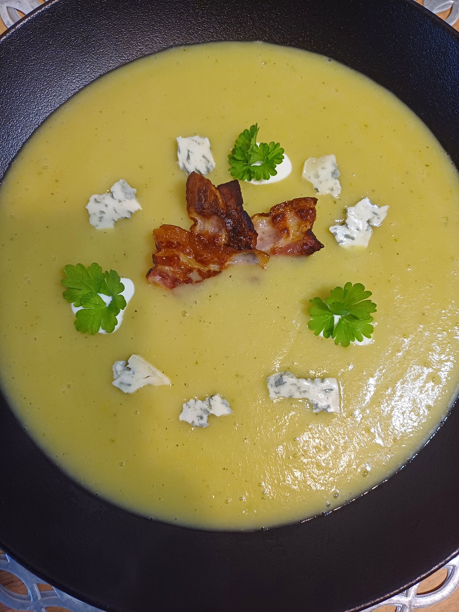 Kremowa zupa w czarnym talerzu, udekorowana serem pleśniowym, boczkiem i natką pietruszki. Eleganckie danie, idealne na wykwintny catering.