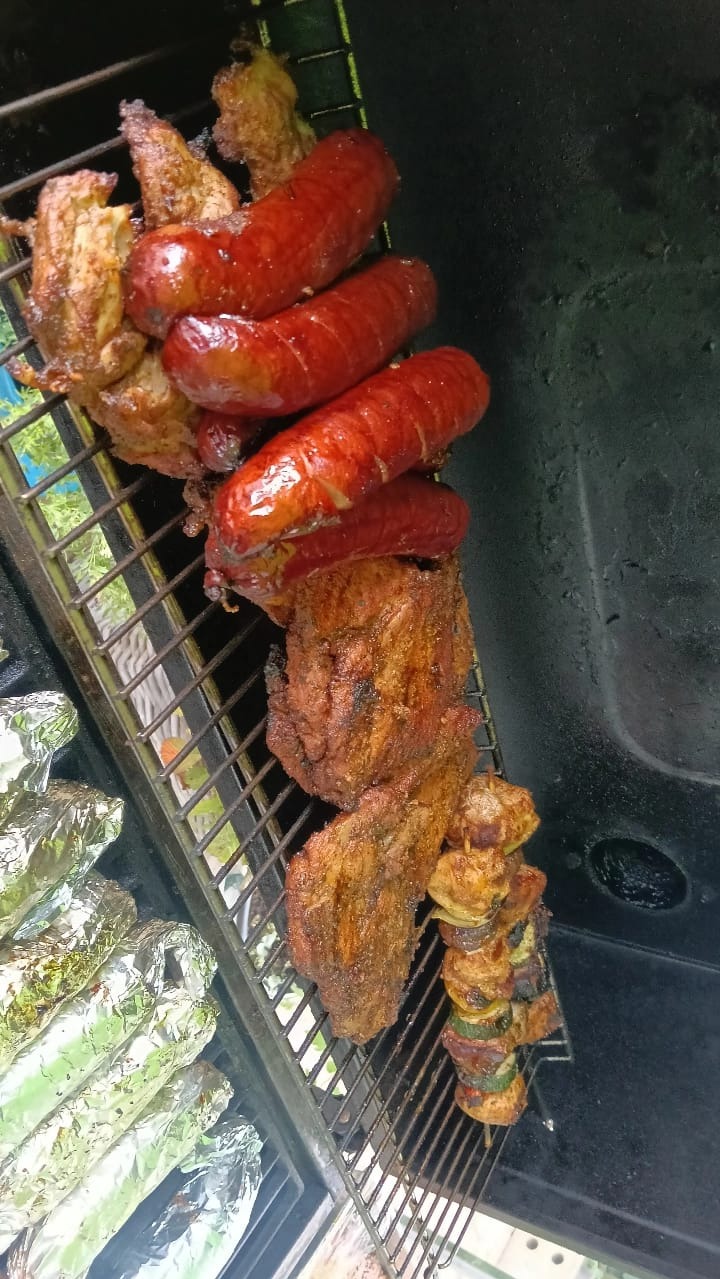 Grill z kiełbasami, mięsem i szaszłykami, obok kukurydza w folii. Widok z góry na ruszt z różnorodnymi, grillowanymi potrawami na przyjęcie plenerowe.