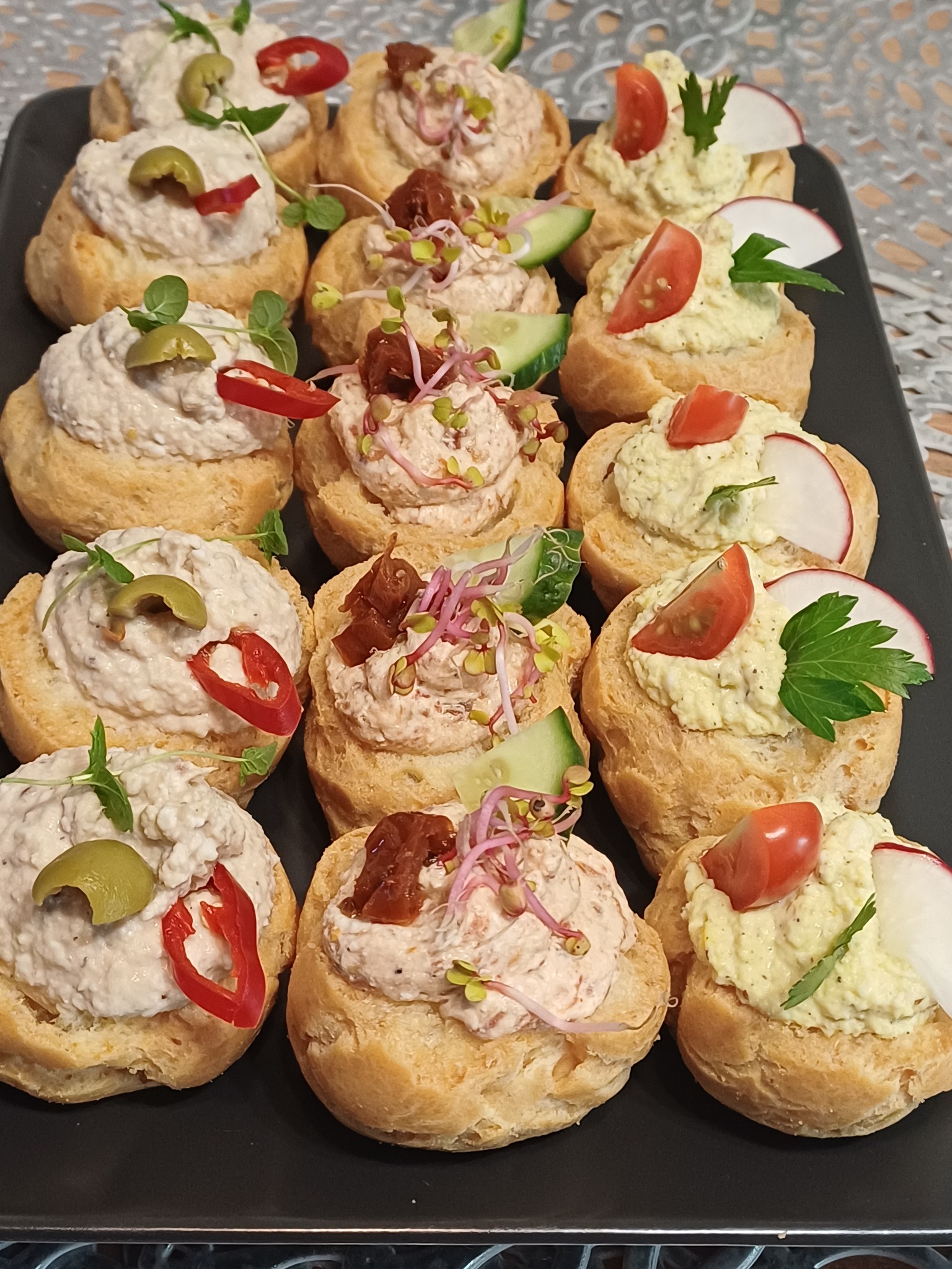 Czarna taca z apetycznymi, różnorodnymi tartaletkami. Kremowe nadzienia zdobione warzywami, ziołami i kiełkami. Idealne na catering.