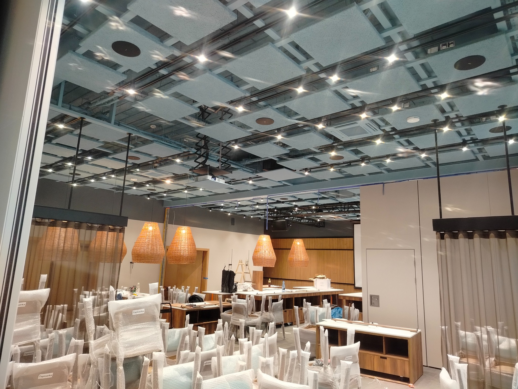 Sufit z panelami akustycznymi i oświetleniem punktowym w nowym lokalu, krzesła w folii ochronnej, lampy wiszące z wikliny, przygotowania do otwarcia.