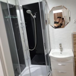 Kacper Cyranski - Nowoczesna kabina prysznicowa z hydromasażem, umywalka z szafką w jasnej łazience. W lustrze odbija się osoba robiąca zdjęcie.