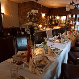 Estera Kołodziej - Uroczysty stół z białym obrusem, zastawą i dekoracjami kwiatowymi w restauracji o kamiennych ścianach, przygotowany na przyjęcie.