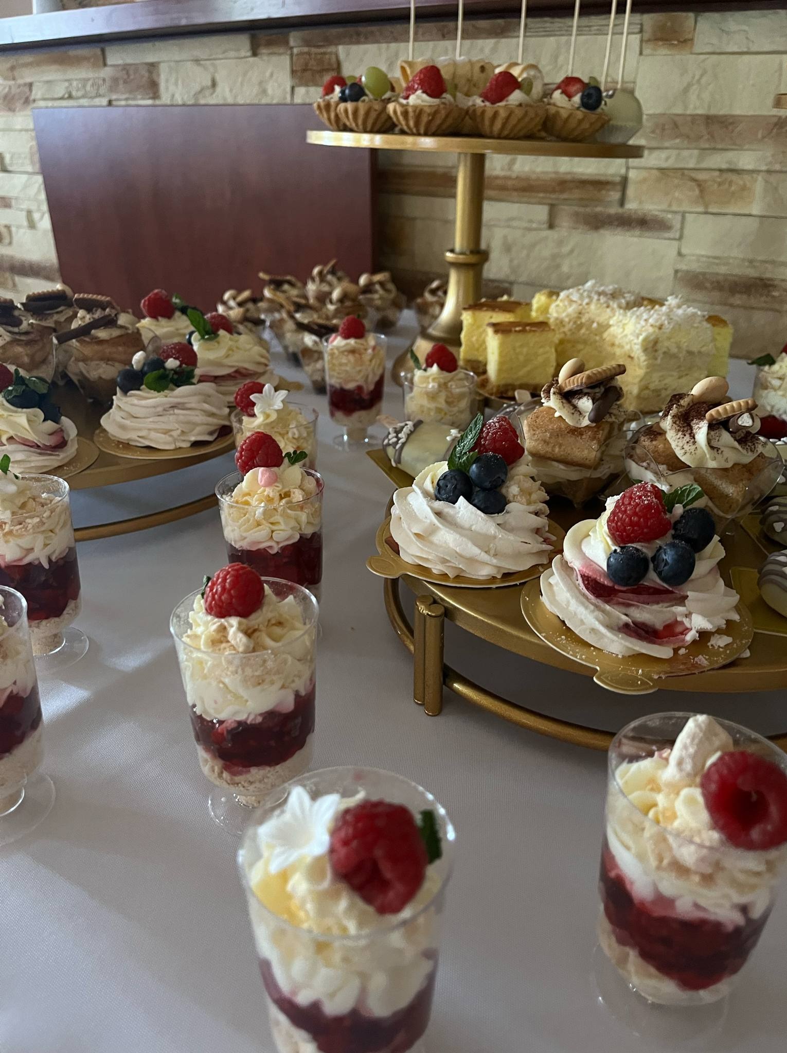 Stół z różnorodnymi deserami: mini bezy z owocami, ciasta i desery w szklankach, tworzące elegancką kompozycję cateringową na przyjęcie.