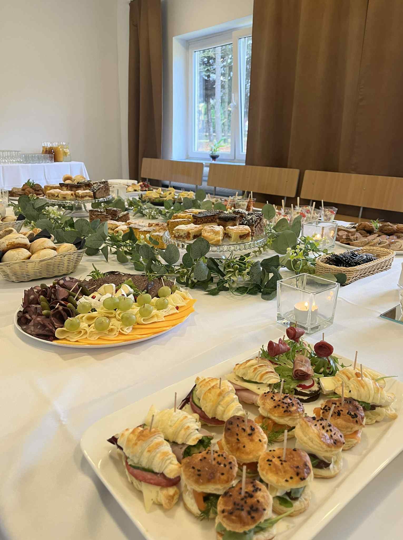 Stół cateringowy z przekąskami: mini burgery, croissanty, sery, wędliny i ciasta, udekorowany zielenią. Usługi cateringowe w Jaworzno.