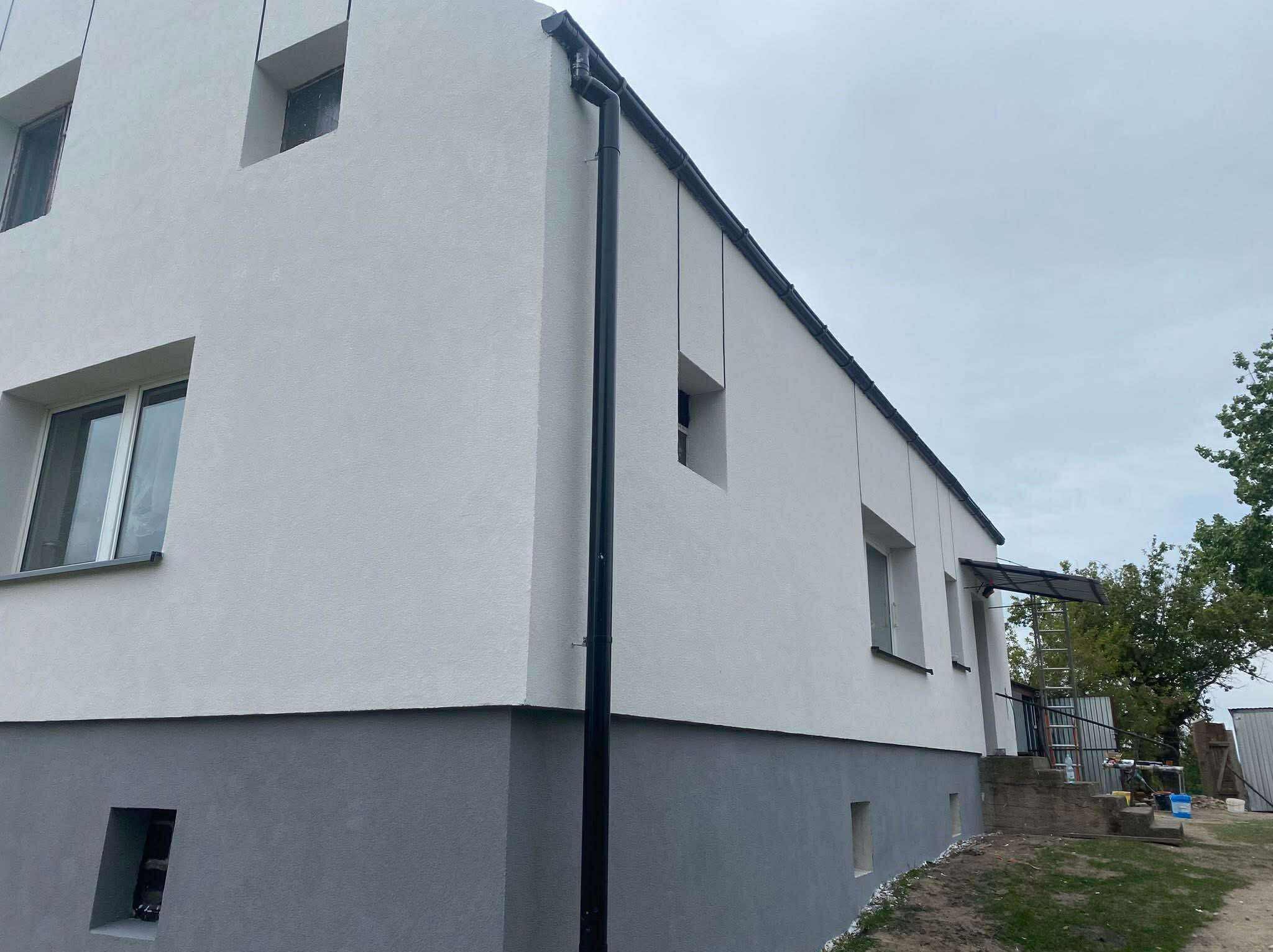 Dwukondygnacyjny budynek po remoncie elewacji, z widoczną nową, dwukolorową strukturą tynku i orynnowaniem. Ujęcie z dołu, pochmurne niebo.
