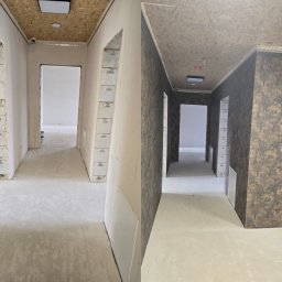 Haj-Bud - Korytarz w trakcie prac wykończeniowych: ściany częściowo z gładzią, częściowo z tapetą o wzorze kamienia. Sufit z płyty OSB. Widoczne otwory drzwiowe.