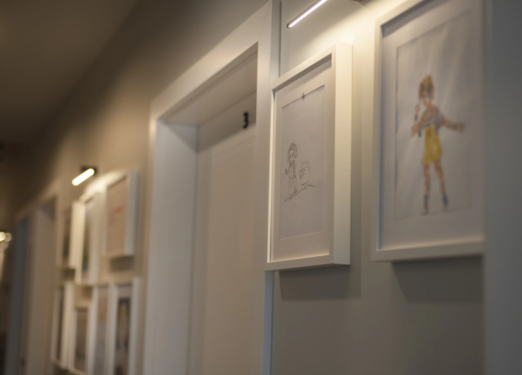 Korytarz w neutralnych barwach z ramkami dziecięcych rysunków na ścianie, oświetlony ledowymi lampami. Widoczny numer 3 na drzwiach.