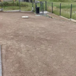 Przygotowany teren pod trawnik z widoczną taczką, zrolowaną trawą i nowym ogrodzeniem. W tle domy w zabudowie szeregowej.