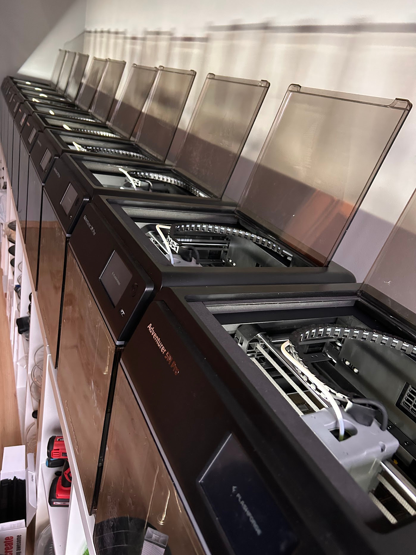 Rząd drukarek 3D Flashforge Adventurer 5M Pro z otwartymi pokrywami, ustawionych na białej półce. Widoczne detale wnętrza drukarek i elementy robocze.