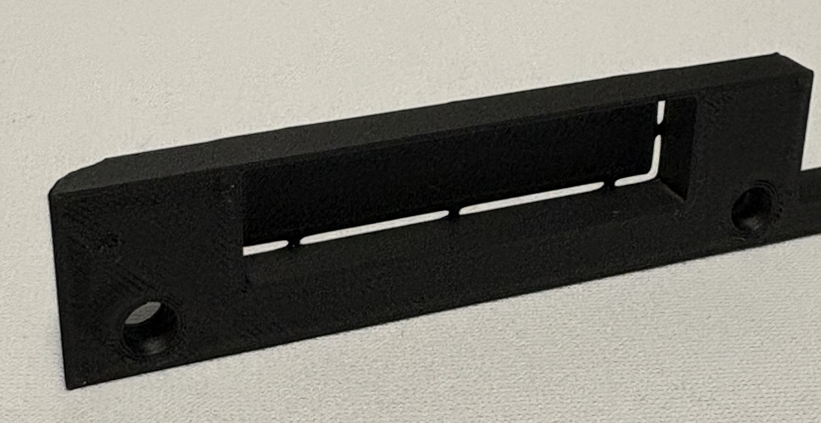 Czarny, matowy element z tworzywa sztucznego z otworami i szczelinami, wykonany w Gdyni. Widoczna faktura materiału.