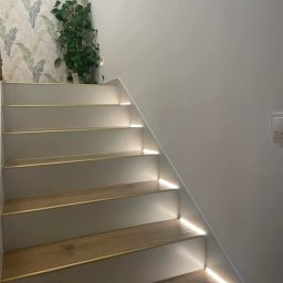 XTEAM - Podświetlane schody z drewnianymi stopniami i subtelnym oświetleniem LED, umieszczonym pod każdym stopniem, tworzącym nowoczesny i elegancki efekt wizualny.