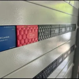 Szara szafa sterownicza z modułami: niebieski TDK-Lambda DRL60-24-1, czerwony Grenton CLU Z-Wave i szare moduły z etykietami. Widoczne diody sygnalizacyjne.