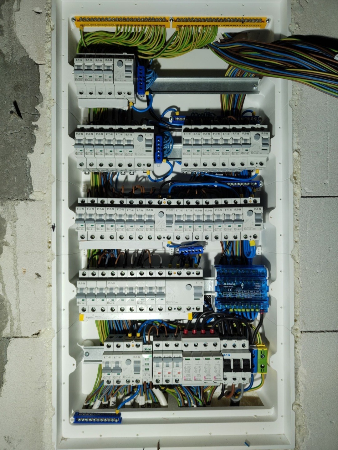 Rozdzielnica elektryczna z zainstalowanymi bezpiecznikami i przewodami w białej obudowie, zamontowana na surowej ścianie z betonu komórkowego.