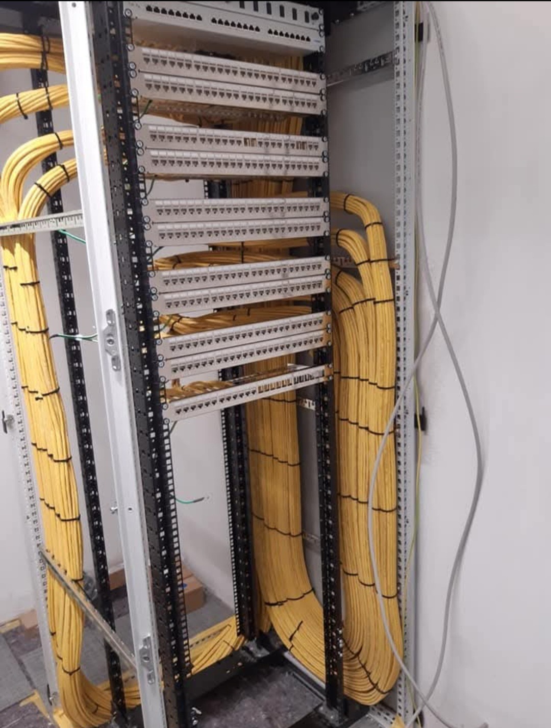 Szafa krosownicza z uporządkowanymi kablami sieciowymi w kolorze żółtym, zamocowanymi w metalowej ramie. Widoczne panele krosownicze i prowadnice kablowe.