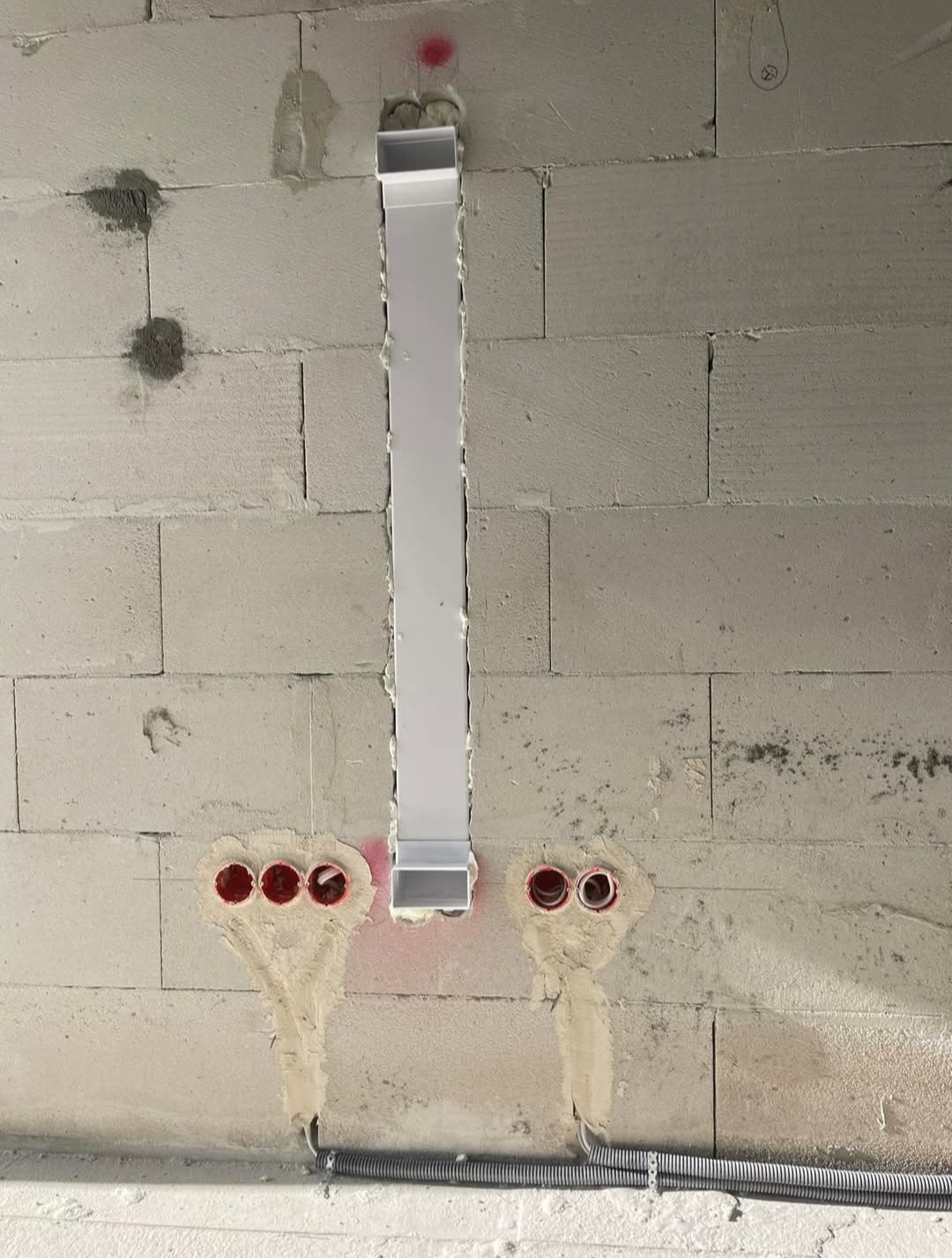 Instalacja elektryczna w ścianie z betonu komórkowego: rura instalacyjna i puszki pod gniazdka, zabezpieczone gipsem. Widoczne przewody w peszlu.