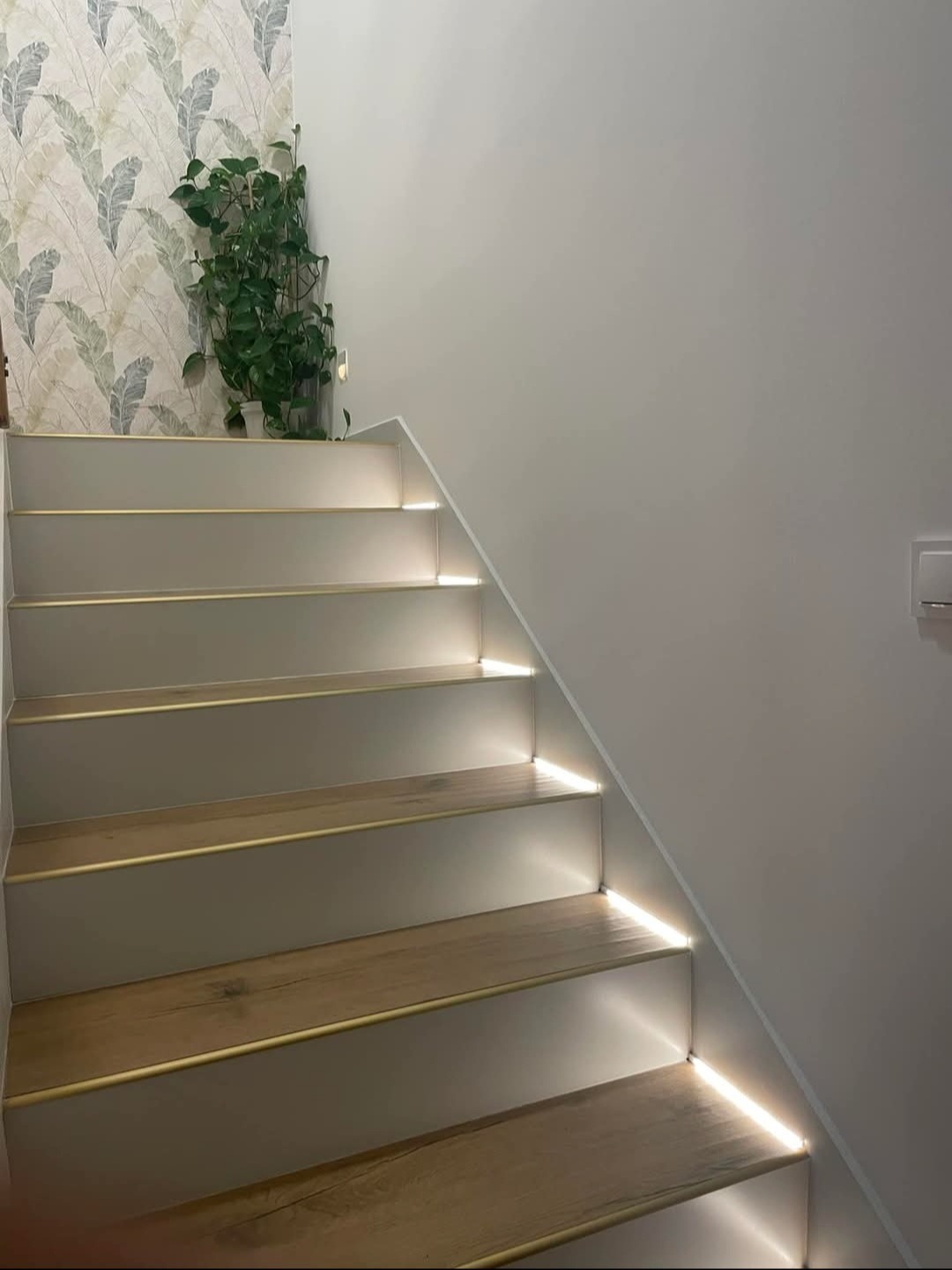 Podświetlane schody z drewnianymi stopniami i subtelnym oświetleniem LED, umieszczonym pod każdym stopniem, tworzącym nowoczesny i elegancki efekt wizualny.