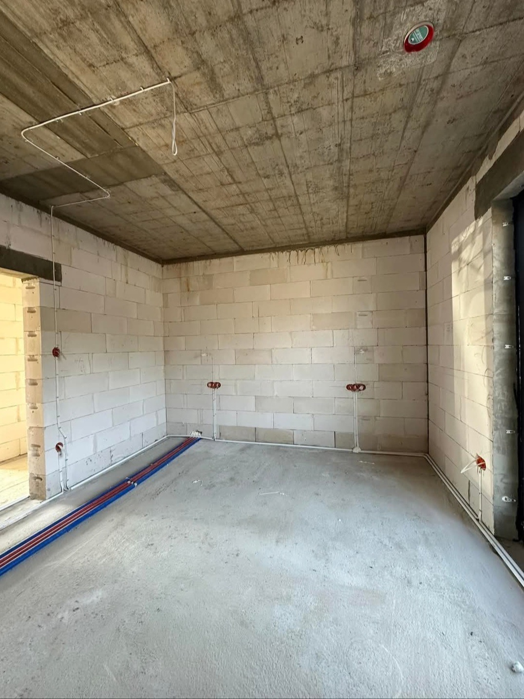Surowy stan wnętrza: ściany z betonu komórkowego, instalacje elektryczne w rurkach, surowy betonowy strop z widocznymi przewodami. Etap prac instalacyjnych.