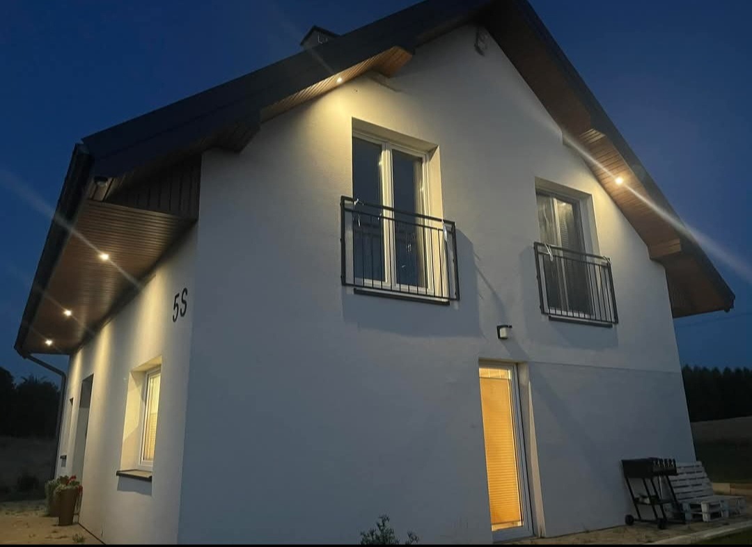 Oświetlenie zewnętrzne domu z numerem 55 w Katowicach, z lampami punktowymi pod okapem, widok nocą.