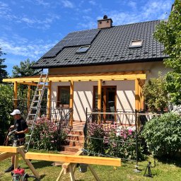 Ontera Design & Build - Konstrukcja drewniana werandy przy domu jednorodzinnym w słoneczny dzień. Stolarz przy pracy, widoczne narzędzia i elementy konstrukcyjne.