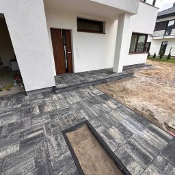 MAKOST BRUKARSTWO - Ułożona, grafitowa kostka brukowa przed nowoczesnym domem. Widoczny fragment wykopu pod dalsze prace. W tle drugi budynek.