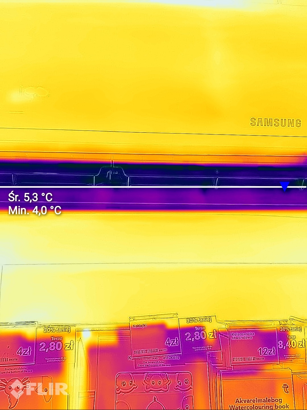 Termowizyjne zdjęcie klimatyzatora Samsung, ukazujące rozkład temperatur. Widoczne wartości średniej i minimalnej temperatury. Dolna część kadru z książkami.