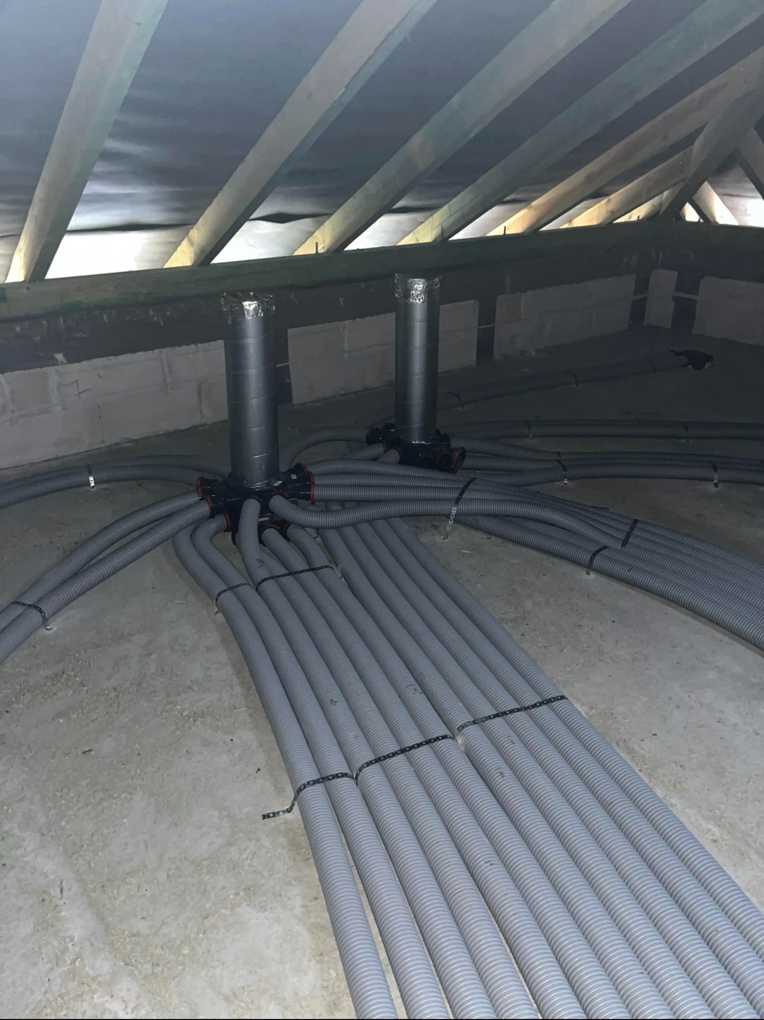 Instalacja wentylacyjna na poddaszu: rury spiro pod stropem, połączone z centralą wentylacyjną. Szare przewody ułożone równolegle, widoczne elementy montażowe.