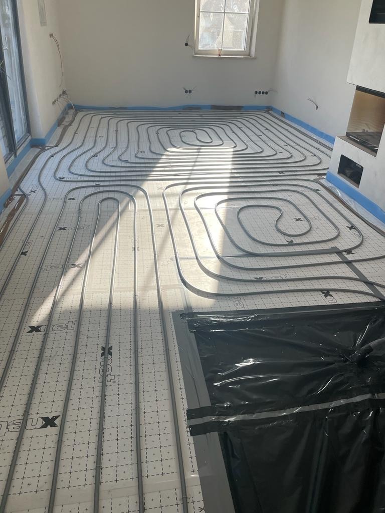 Ułożona instalacja ogrzewania podłogowego na macie grzewczej w jasnym pomieszczeniu, widoczne rury w kształcie pętli, przygotowane do zalania posadzką.