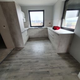 Perfect Design Grzegorz Siudak - Jasna kuchnia w stylu nowoczesnym z drewnopodobną podłogą i czarną armaturą. Widoczny fragment niezabudowanej ściany.