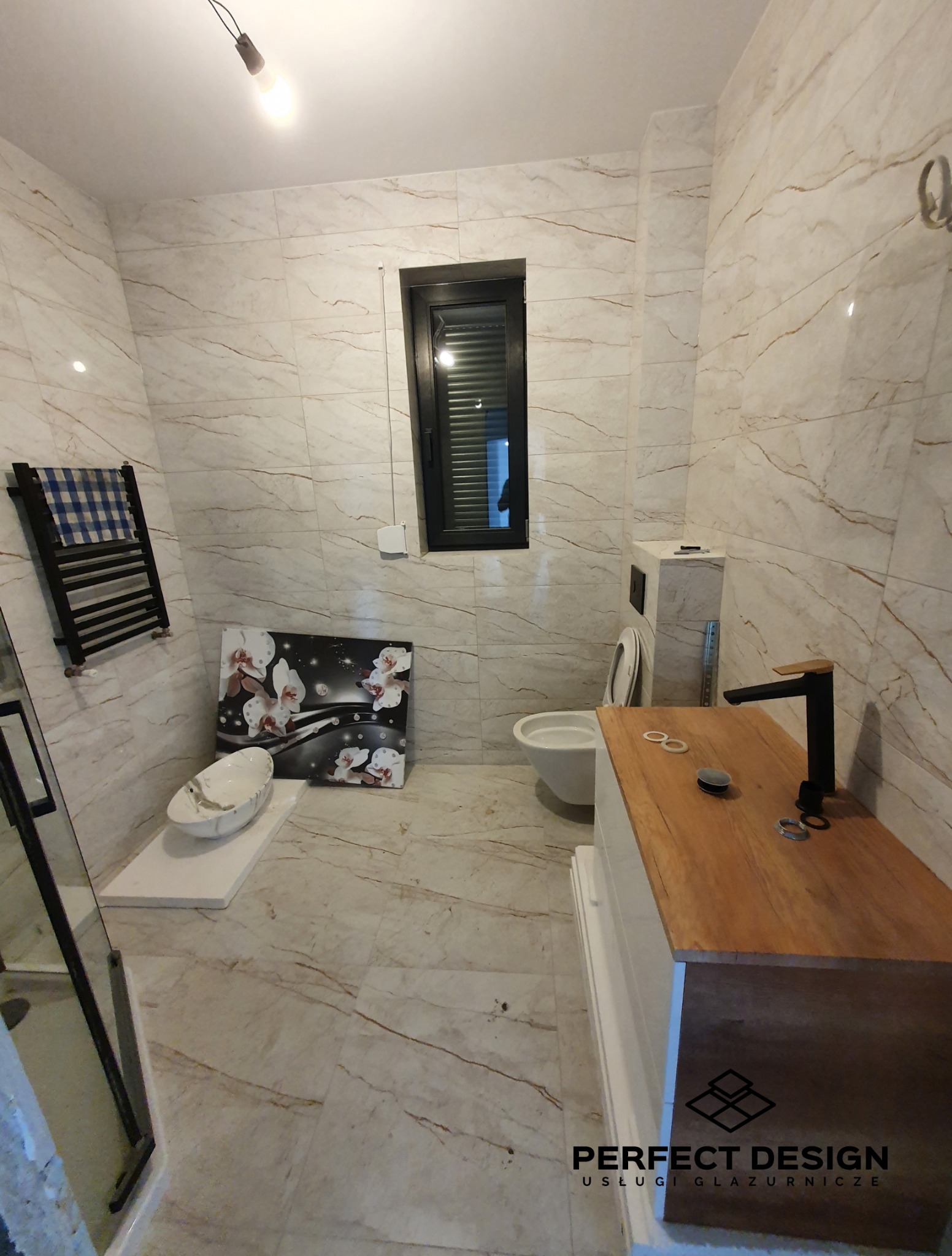 Nowoczesna łazienka z marmurowymi płytkami, czarną armaturą i oknem. Umywalka nablatowa i dekoracyjny obraz z motywem kwiatowym dodają elegancji.