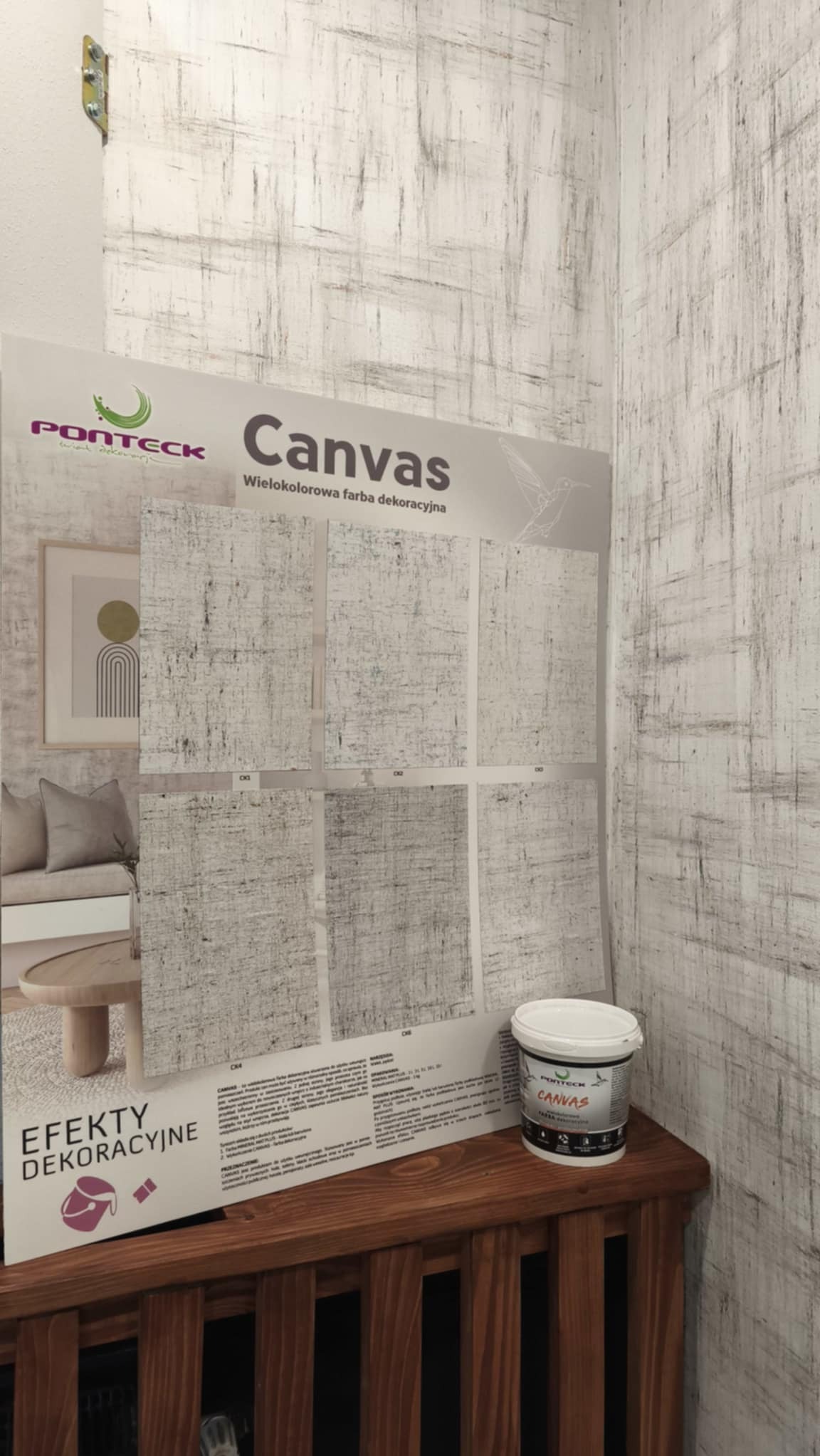 Wielokolorowa farba dekoracyjna Canvas marki Ponteck na tle ściany z efektem dekoracyjnym. Prezentacja próbek i puszka farby na drewnianej komodzie.