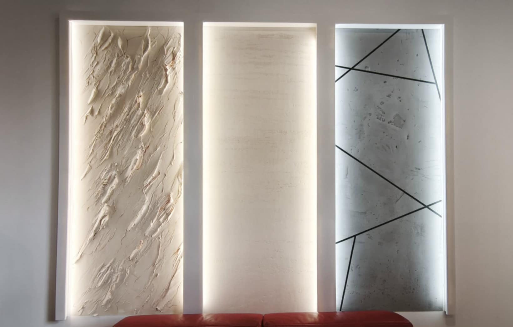 Dekoracyjne panele ścienne z różnymi fakturami i wzorami, podświetlone pionowym światłem, umieszczone nad czerwoną sofą w nowoczesnym wnętrzu.