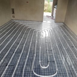 Hydrodzięcioł Usługi Hydrauliczne Łukasz Trzebiatowski - Ułożona instalacja ogrzewania podłogowego na folii z nadrukiem 'KELLER' w surowym wnętrzu, widok z góry, przygotowana do zalania posadzką.