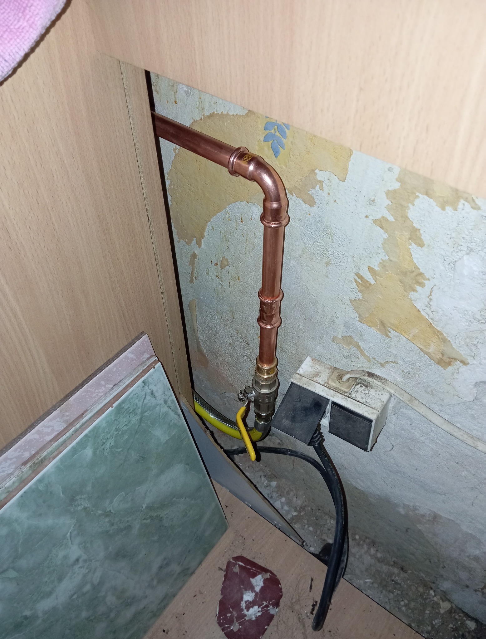 Miedziana instalacja gazowa z żółtym zaworem, widoczna przyłączeniowa rura gazowa w pomieszczeniu z fragmentami starej tapety.