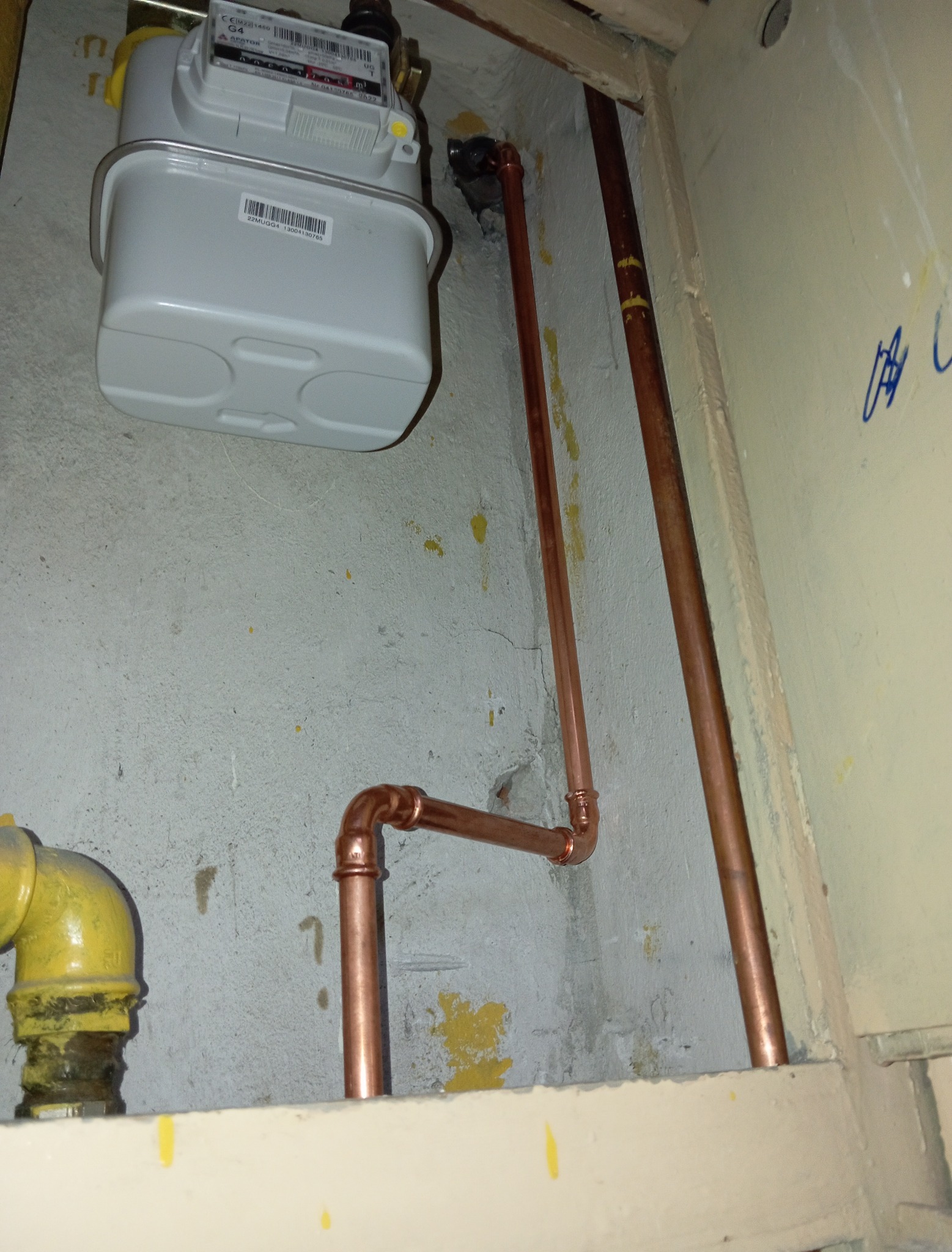 Zamontowany gazomierz z nową instalacją z rur miedzianych. Żółty zawór gazowy po lewej stronie. Ściana z widocznymi śladami po instalacji.