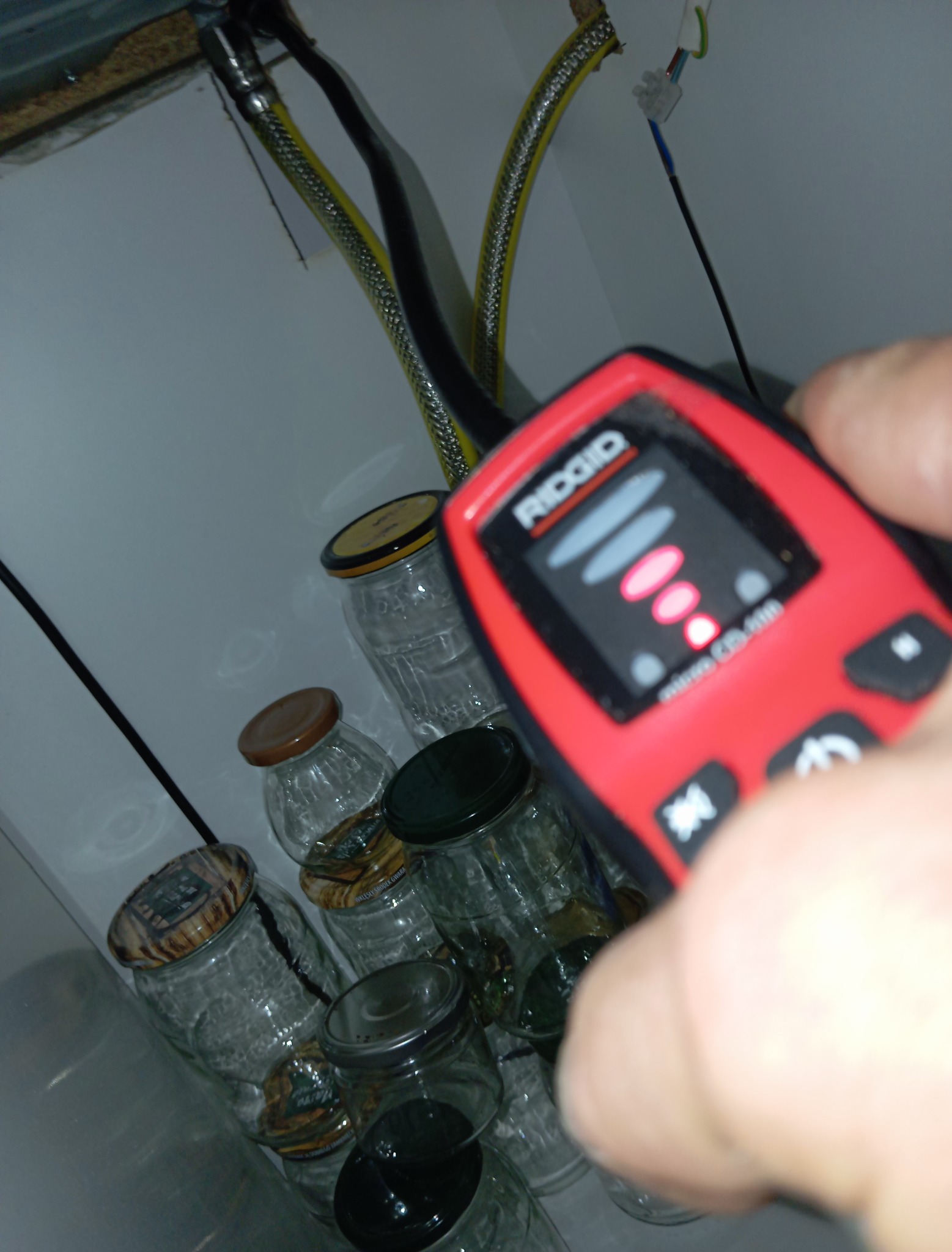 Próba szczelności instalacji gazowej detektorem RIDGID micro CD-100 w pomieszczeniu z słoikami. Widoczne rury instalacji gazowej.