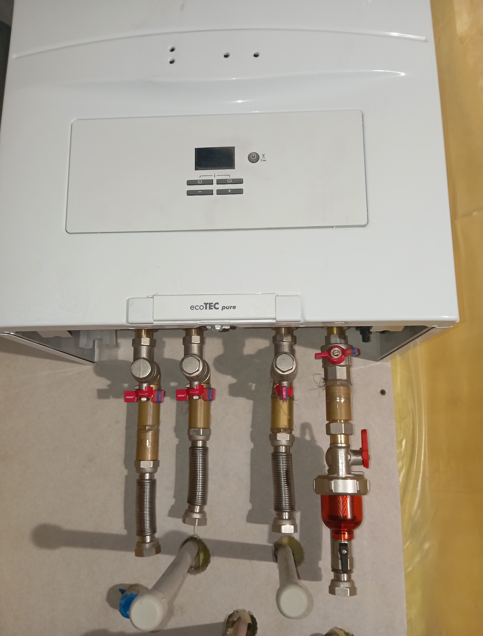 Biały piec gazowy Vaillant ecoTEC pure z podłączonymi rurami i zaworami. Widoczne elementy instalacji gazowej, filtr z czerwoną obudową.