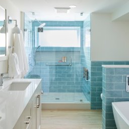 Solidnyfach.gorzow - Jasna łazienka z kabiną prysznicową w turkusowej glazurze, drewnopodobną podłogą i białymi meblami. Nowoczesny design z oknem w kabinie.