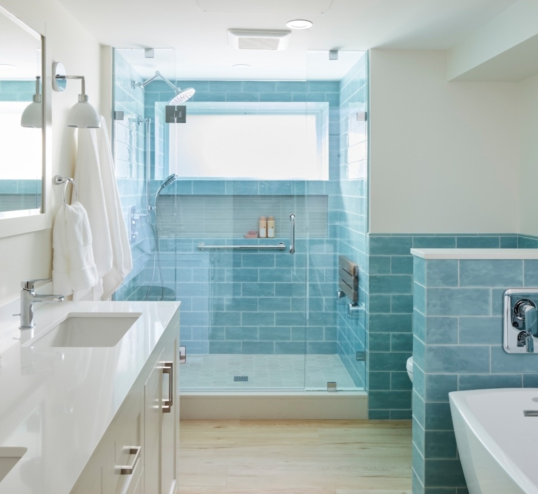 Jasna łazienka z kabiną prysznicową w turkusowej glazurze, drewnopodobną podłogą i białymi meblami. Nowoczesny design z oknem w kabinie.