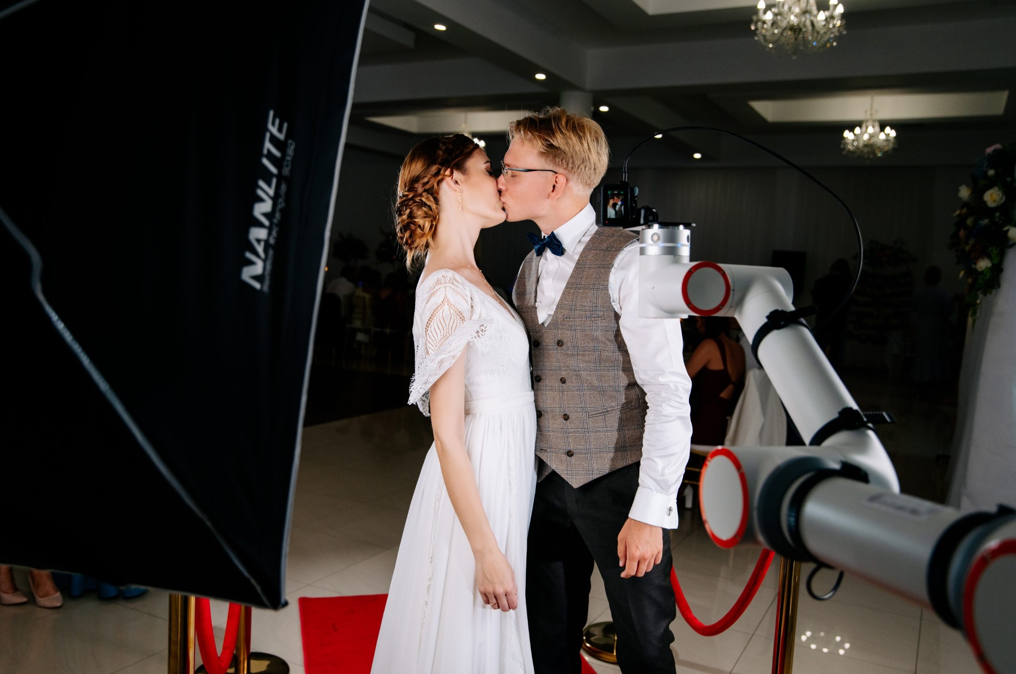 Para młoda całuje się przed robotem filmowym Glambot na tle softboxu Nanlite i czerwonego dywanu, tworząc pamiątkę z imprezy w stylu Hollywood.