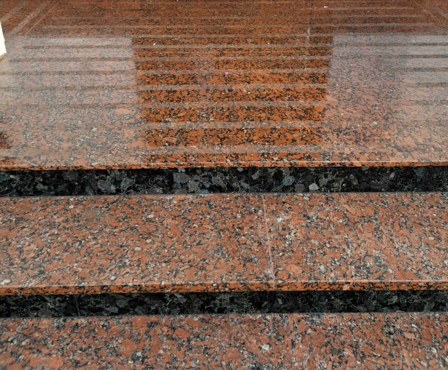 Granitowe schody zewnętrzne w odcieniach czerwieni i czerni, z widoczną strukturą kamienia i refleksami światła na powierzchni.