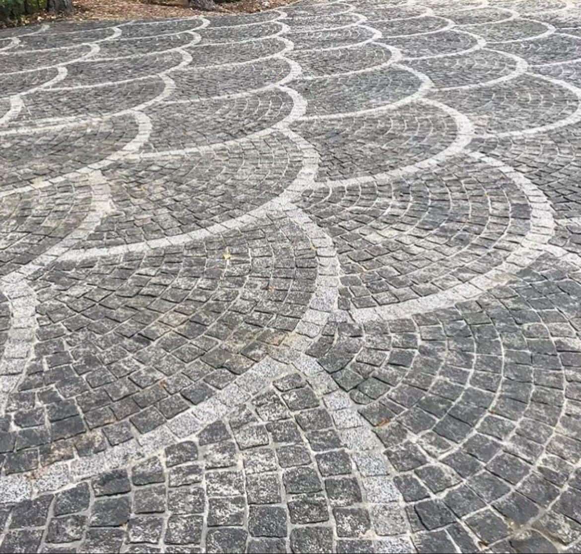 Ułożona kostka granitowa w dekoracyjny wzór wachlarza z jasnymi obwódkami. Szara kostka tworzy regularny, powtarzalny deseń na dużej powierzchni.